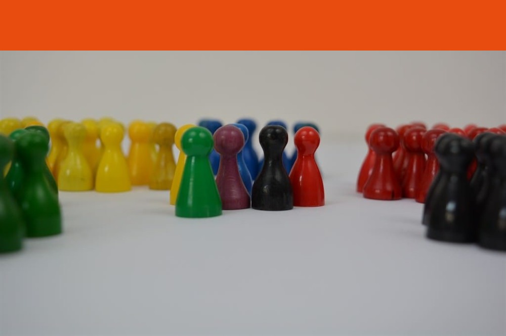 Bunte Spielfiguren stehen in mehreren Gruppen nebeneinander, in der Mitte eine gemischte Gruppe aus grüner, violetter, schwarzer und roter Figur